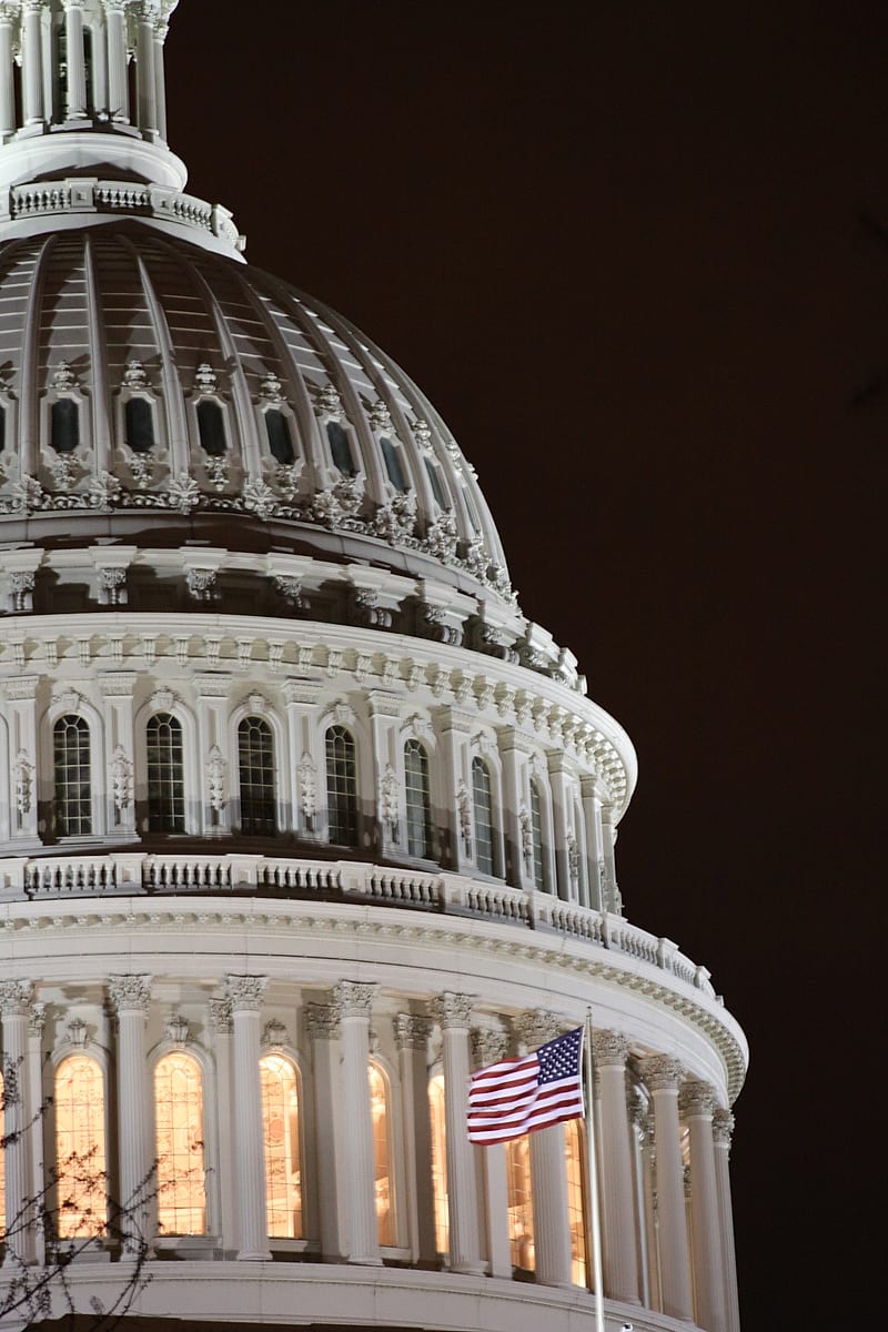 The U.S. Capitol dome lit at night beside the flag
