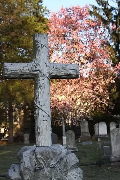 A weathered cross headstone with autumn color behind it