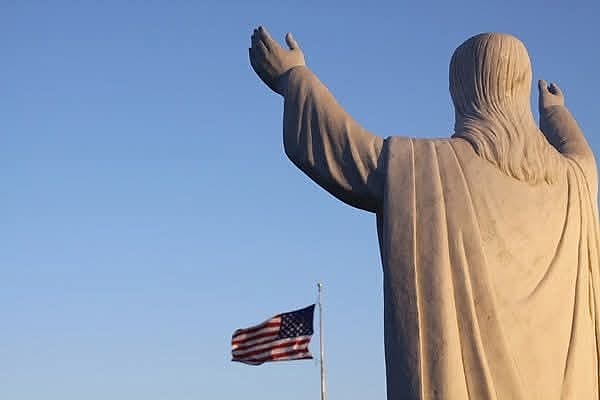 A statue reaching skyward with an American flag beyond