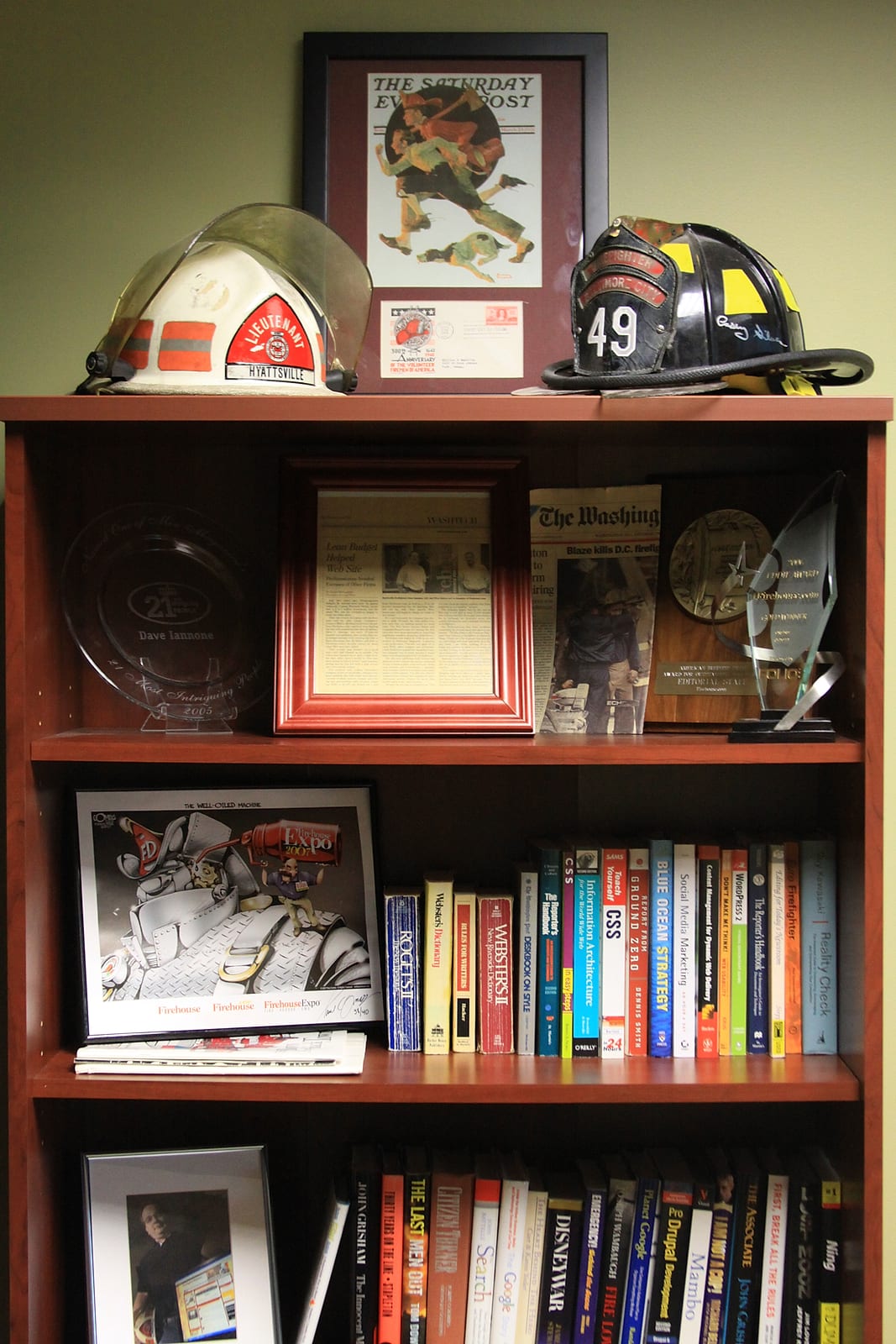 A shelf of fire helmets, awards and books in Dave's office