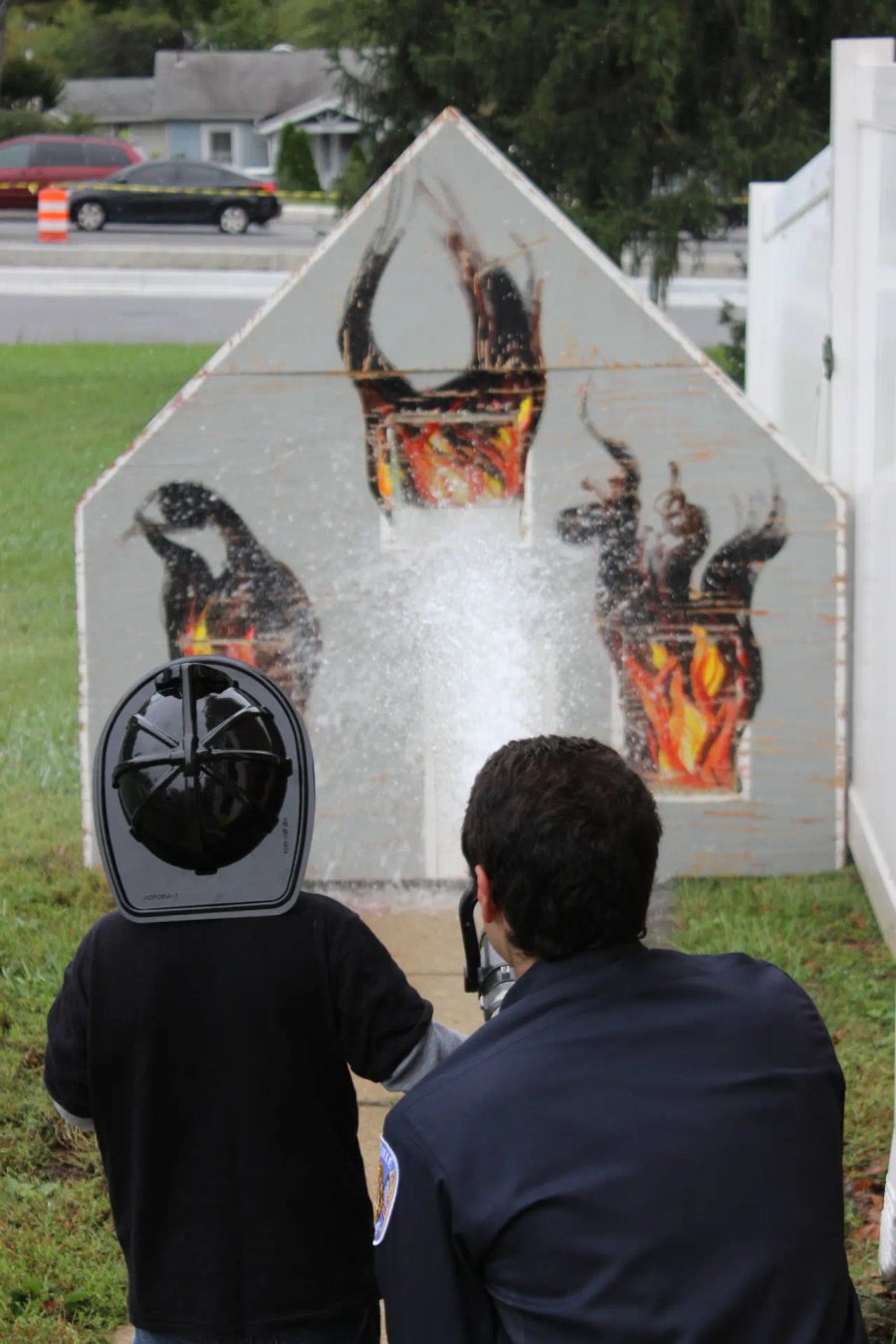 A child aims a fire hose at a flame prop during a firehouse open house